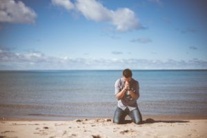 Man praying on knees at the beach